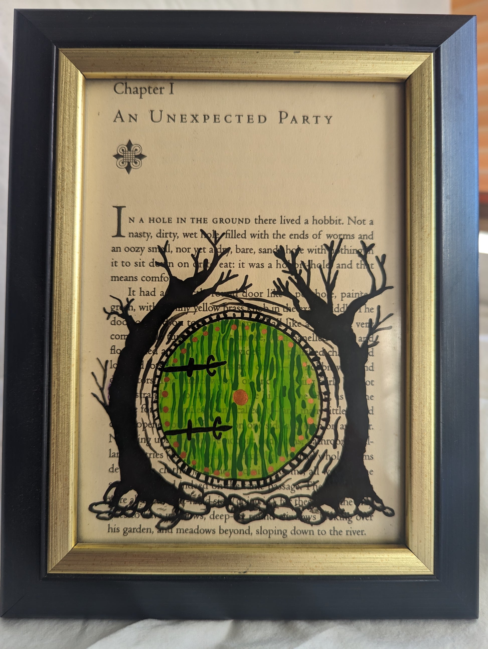 "An Unexpected Party" is 5x7 inches in a gold rimmed felt backed frame that can be wall hung or table displayed. Features the first page of Chapter 1 from Tolkien's "The Hobbit". Bilbo's green door with golden doorknob and surrounding black trees is hand painted in reverse on the glass.
